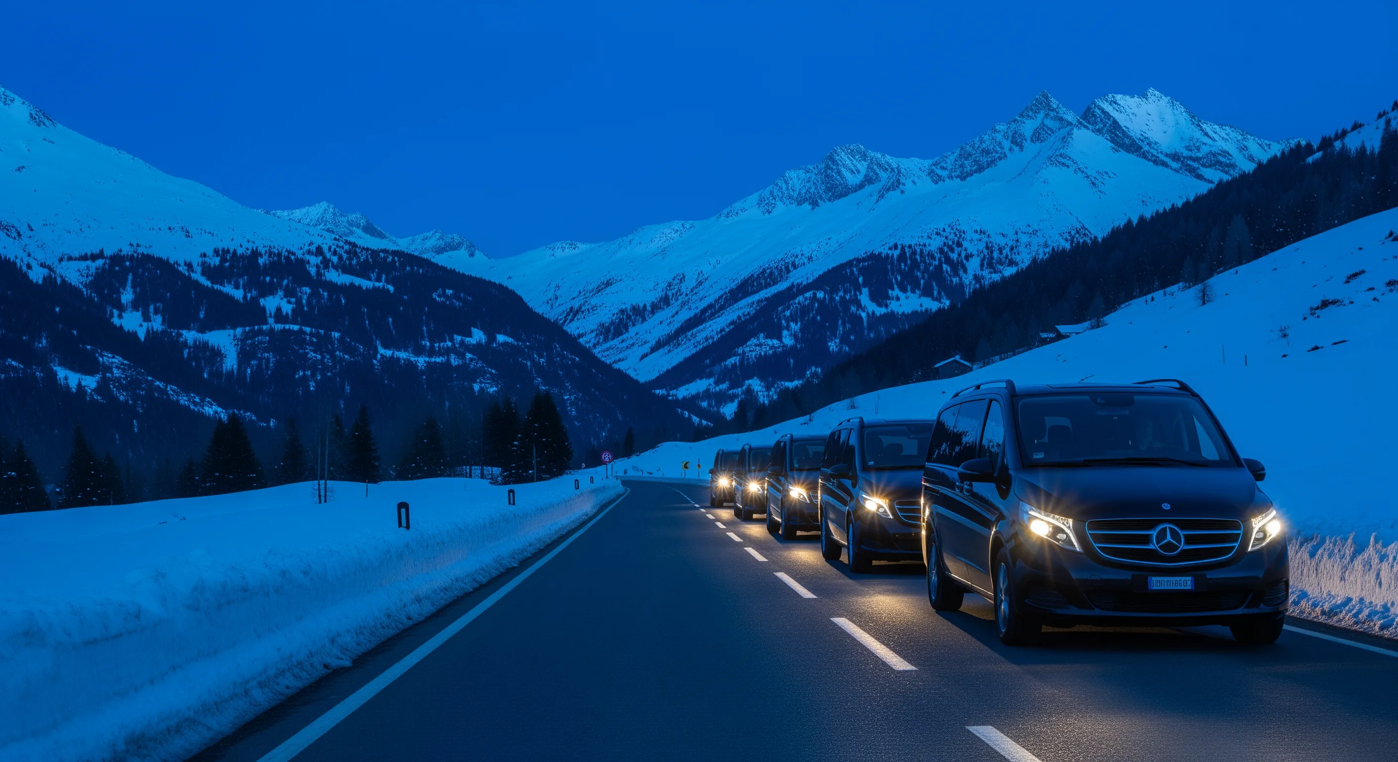 Convoy of Mercedes V-Class vehicles on alpine road at dusk with snowy mountains